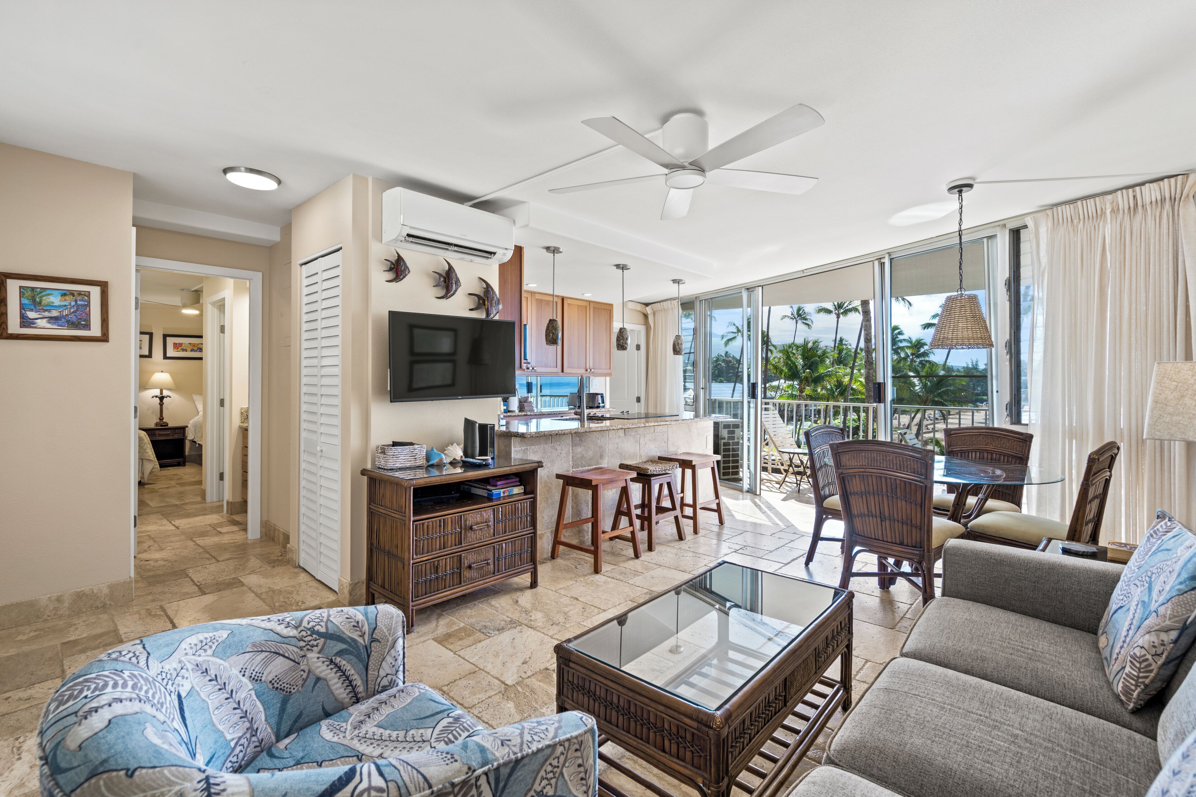 A spacious living area with a glass coffee table, comfortable seating, a flat-screen TV, and a view of the outdoors.