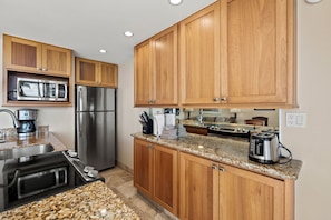 A modern kitchen with wooden cabinets, stainless steel appliances, granite countertops, and a built-in oven. - Your Perfect Ocean View Retreat in a Desirable Location! -Kamaole Nalu #405:  (Kihei, Maui)