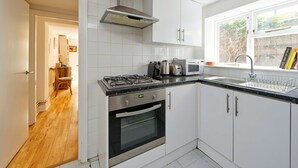 Eine moderne Küche mit weißen Schränken, einem Gasherd, einem Backofen, einer Mikrowelle und einem Fenster mit Blick auf Grünflächen.