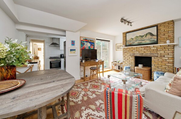 A spacious living area with a fireplace, a dining table with chairs, and a sofa. - Lovely 2 bed Flat With Garden in Queen s Park (London)