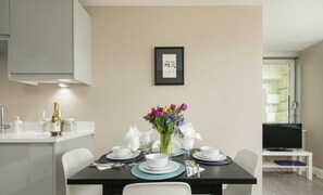 A dining area with a table set for four, a vase with flowers, and a framed picture on the wall. - Gorgeous AP Next to Pier Beach (Brighton)