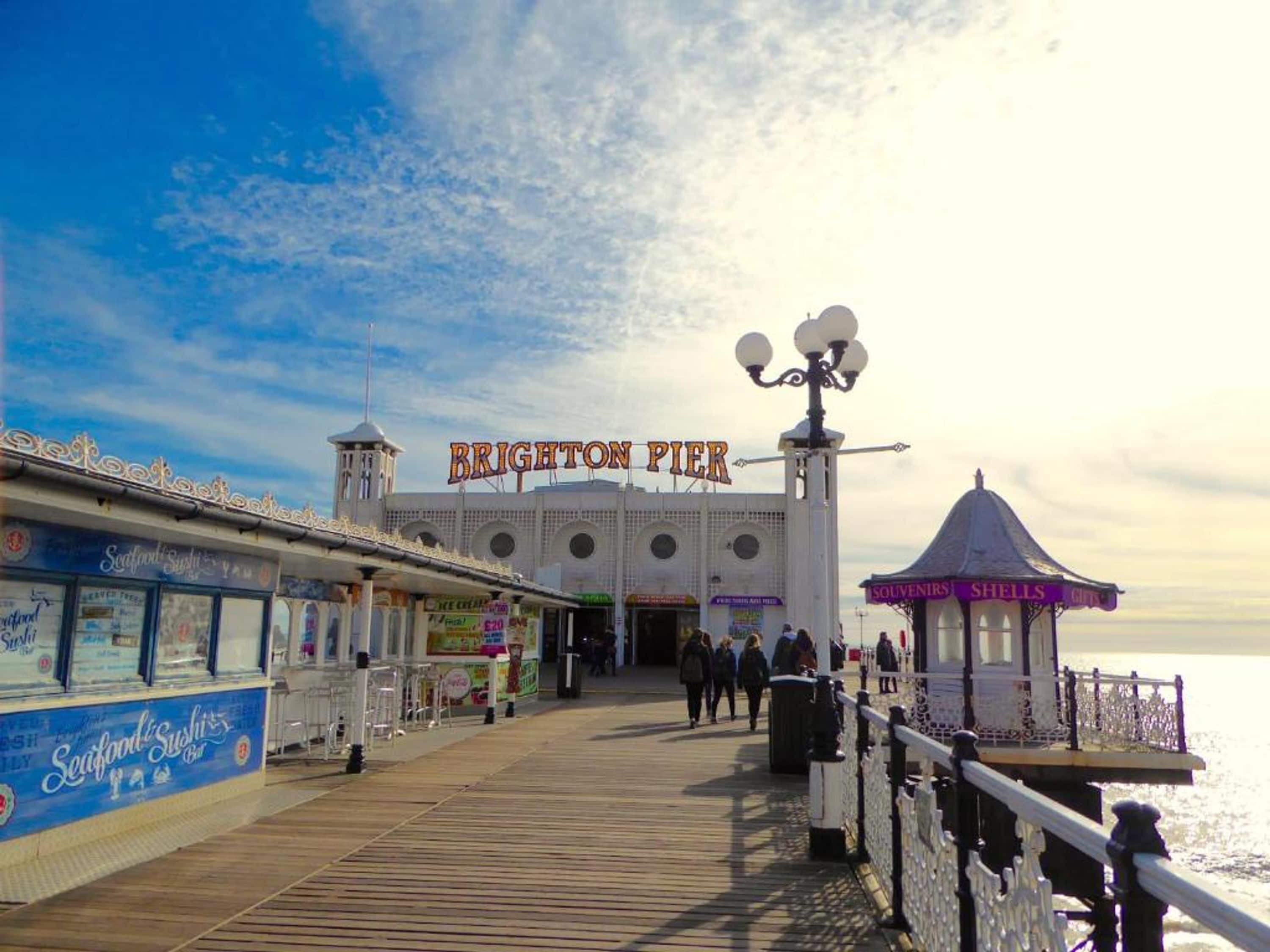 Un muelle con un cartel que dice 'Brighton Pier' y un restaurante de mariscos llamado 'Seafood Sushi Bar'.