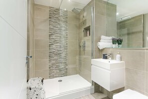 A modern bathroom with a glass-enclosed shower, a white vanity, and a large mirror. - Gorgeous AP Next to Pier Beach (Brighton)