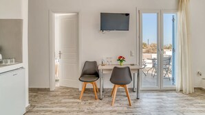 A modern kitchen with a built-in refrigerator, a dining area with two chairs and a table, a flat-screen TV mounted on the wall, and a sliding glass door leading to an outdoor patio. - Venus s Seaside Bliss - Paros Dream Haven (Paros)