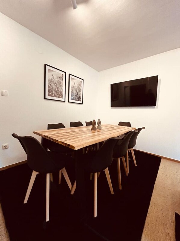 Ein Konferenzraum mit einem Holztisch, schwarzen Stühlen, zwei gerahmten Bildern und einem Flachbildfernseher an der Wand.