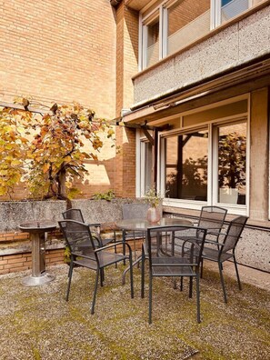Eine Außenpatio mit einem runden Tisch und Stühlen, einer kleinen Vase mit Blumen und einem Baum mit Herbstlaub.