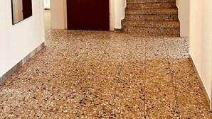 Un couloir avec une porte rouge, un escalier et un miroir au mur.