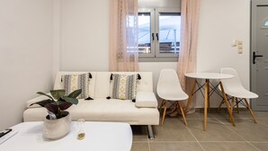Een moderne woonkamer met een bank, twee witte stoelen, een bijzettafeltje en een potplant.