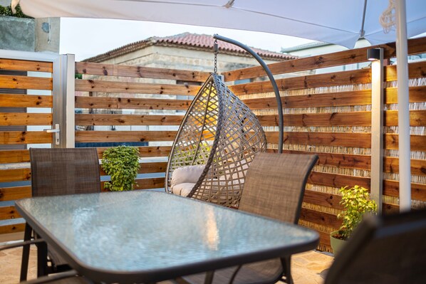 Un patio con una mesa y sillas de metal, una silla colgante y una valla de madera.