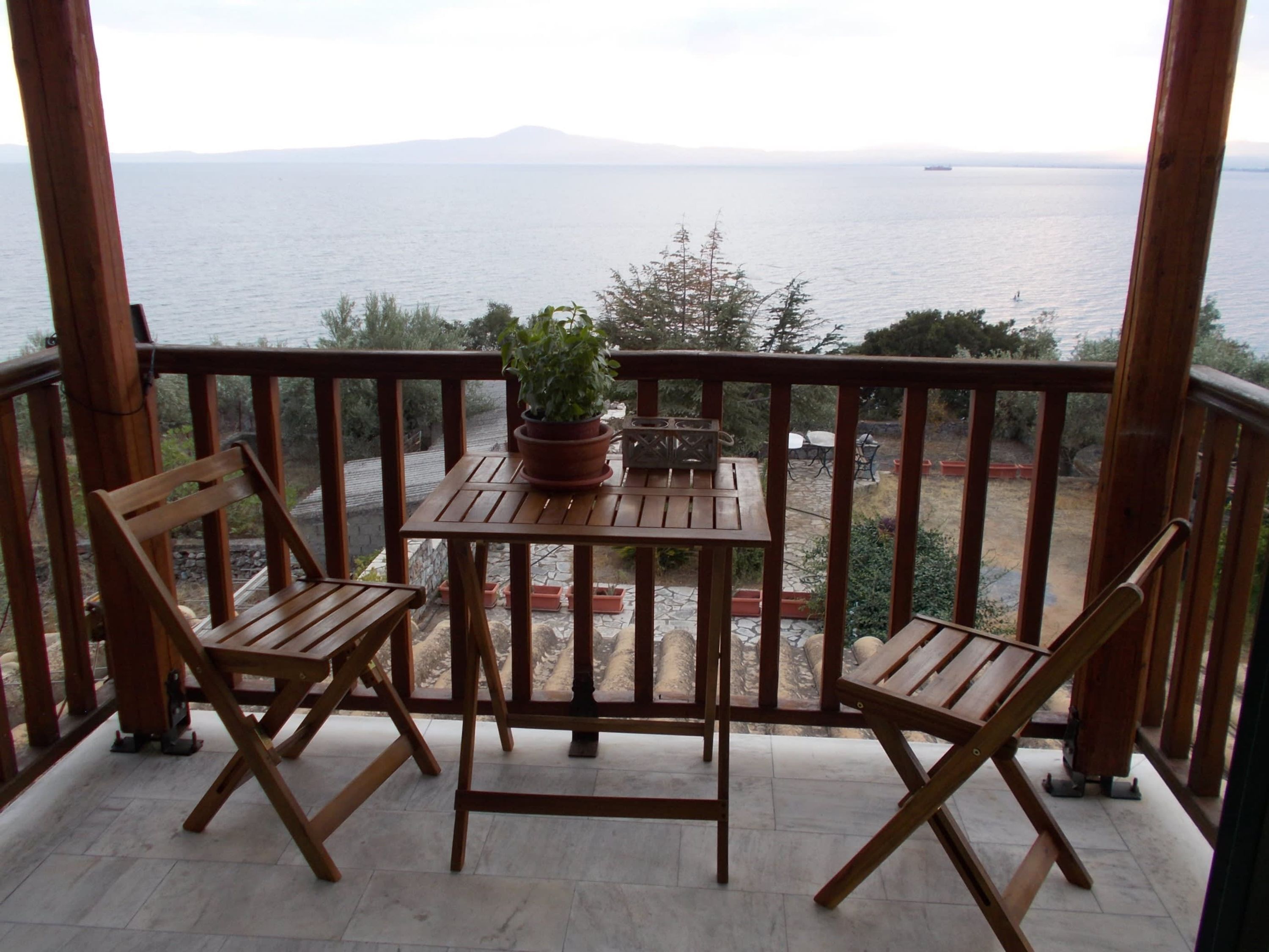A wooden deck with two chairs and a table, overlooking a body of water with a distant mountain.