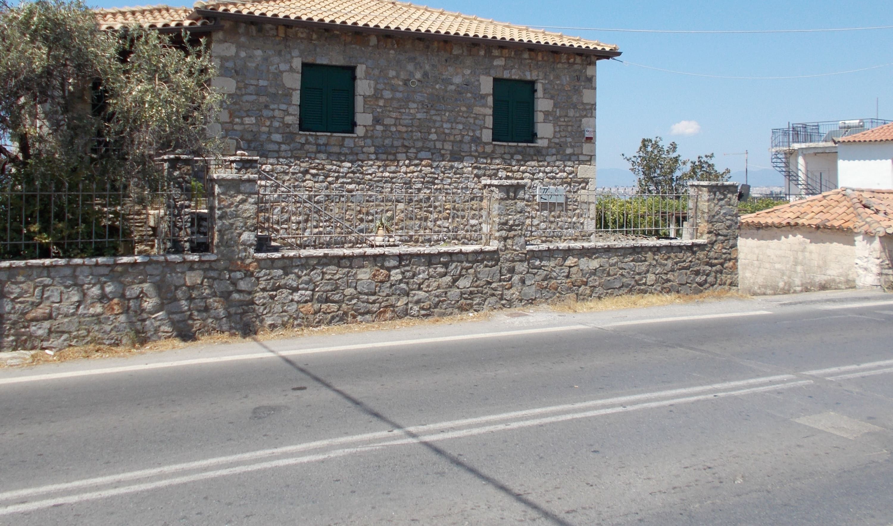 A stone building with two green windows, a metal fence, and a clear sky.
