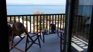A balcony with a view of the sea, wooden chairs, and a table with a hat.