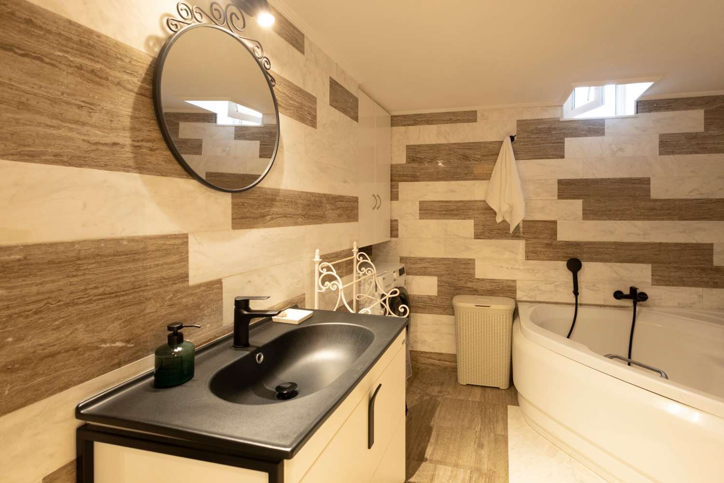 Une salle de bain avec un lavabo noir, un miroir, une baignoire blanche et une serviette accrochée au mur.