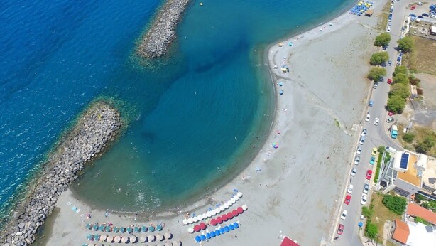 An aerial view of a beach with a rocky shoreline, a row of beach umbrellas, and a road adjacent to the beach. - Kalamata Garden Haven - Escape Amidst Greenery (Kalamata)