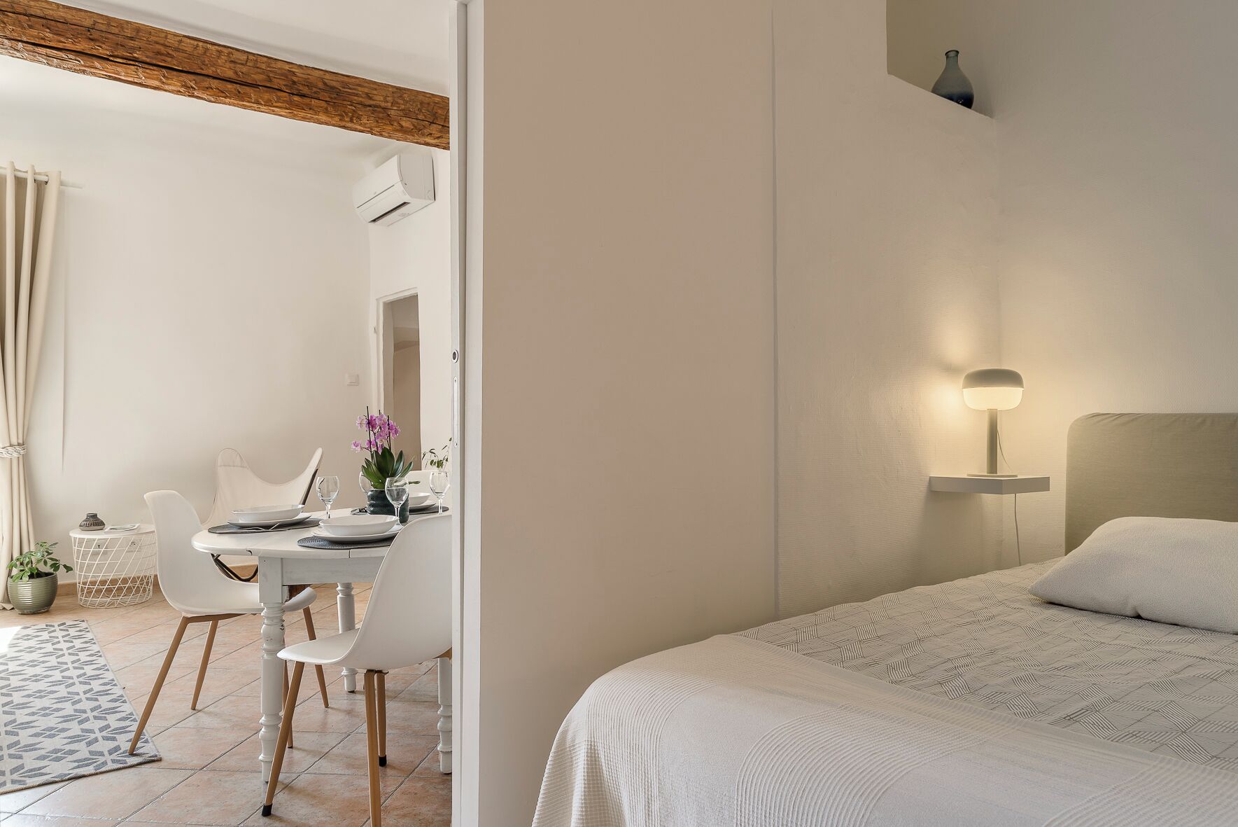 Ein Hotelzimmer mit Bett, Nachttisch mit Lampe, Essecke mit Stühlen und Tisch sowie einer Topfpflanze.
