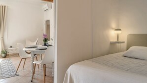 Une chambre d’hôtel comprenant un lit, une table de chevet avec une lampe, un coin repas avec des chaises et une table, et une plante en pot.