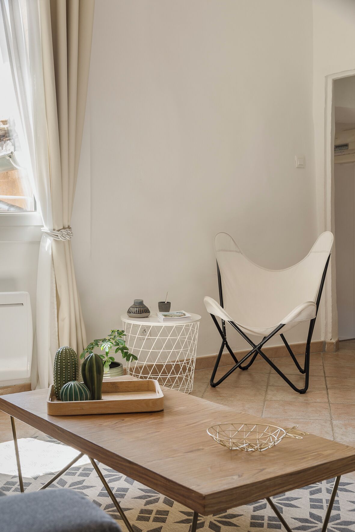 Ein Zimmer mit einem Holztisch, einem weißen Stuhl, einem Kaktus und einem kleinen weißen Beistelltisch mit Dekoration.
