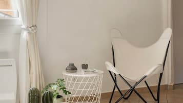 Ein Zimmer mit einem Holztisch, einem weißen Stuhl, einem Kaktus und einem kleinen weißen Beistelltisch mit Dekoration.