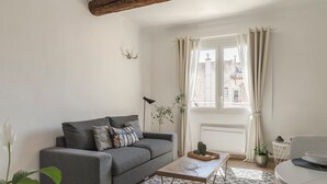 Un salon avec un canapé gris, une table basse, une plante en pot et une fenêtre avec des rideaux.