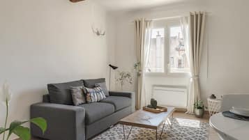 Ein Wohnzimmer mit grauem Sofa, einem Couchtisch, einer Topfpflanze und einem Fenster mit Vorhängen.