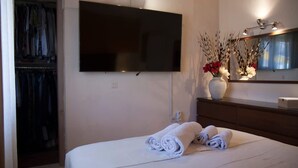 Ein Schlafzimmer mit einem Bett, einem an der Wand befestigten Fernseher, einem Spiegel und einer Vase mit Blumen.