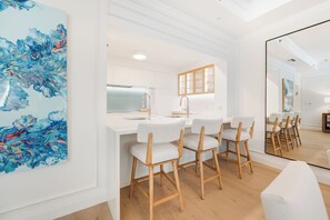 A modern kitchen with white cabinetry, a central island, and bar stools. - Residence 303, Elegant Oasis on Seven Mile Beach (Seven Mile Beach)