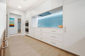 A kitchen with white cabinetry, a built-in oven, and a blue backsplash. - Residence 303, Elegant Oasis on Seven Mile Beach (Seven Mile Beach)