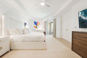 Un dormitorio moderno con una cama grande, un ventilador de techo y vista al océano a través de una puerta corrediza de vidrio.
