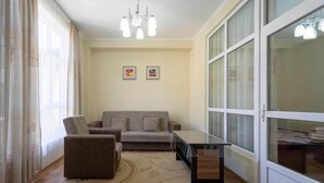 Uma sala de estar com um sofá, uma poltrona e uma mesa de centro. Há duas imagens emolduradas na parede.