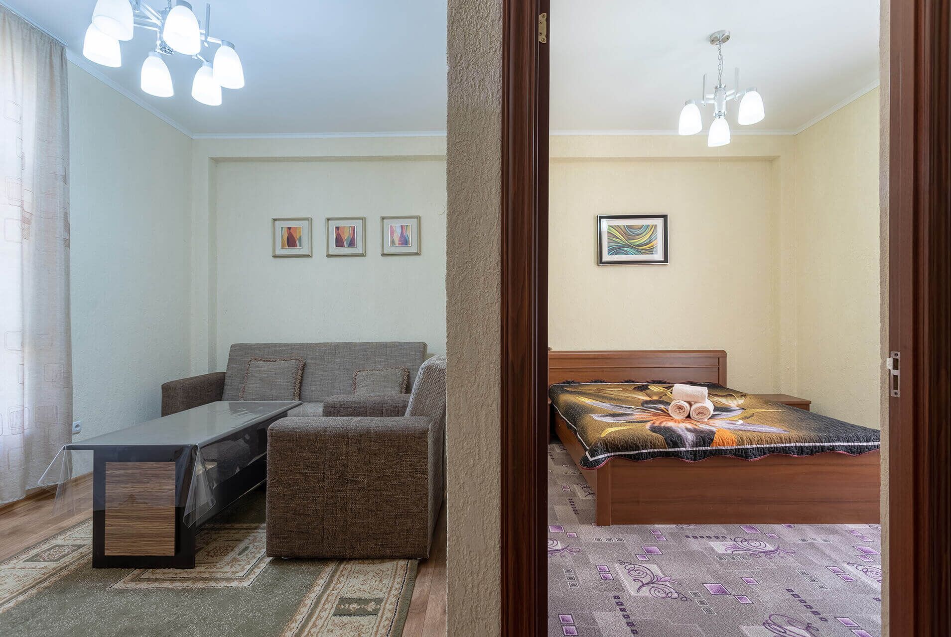 A room with a sofa, a small table, a bed with a patterned bedspread, and a ceiling fan.