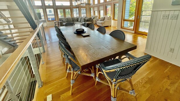 A spacious dining area with a long wooden table, wicker chairs, and a staircase leading to an upper level. - OCEANBLOCK PROPERTY WITH AMAZING DECKS! (Rehoboth Beach)