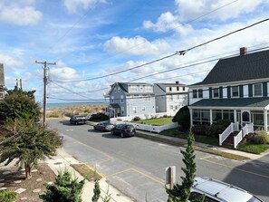 Une rue résidentielle bordée de maisons, avec des voitures garées et une vue dégagée sur l’océan.
