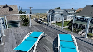 A wooden deck with two blue lounge chairs, a view of the ocean, and residential buildings in the background. - OCEANBLOCK PROPERTY WITH AMAZING DECKS! (Rehoboth Beach)