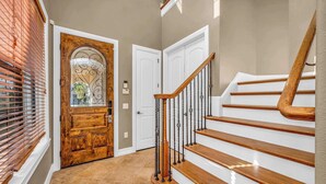 A wooden staircase with white steps and a metal railing, leading to a door with a glass panel. - Bright 5BR retreat w/ pool & fire pit (Kissimmee)