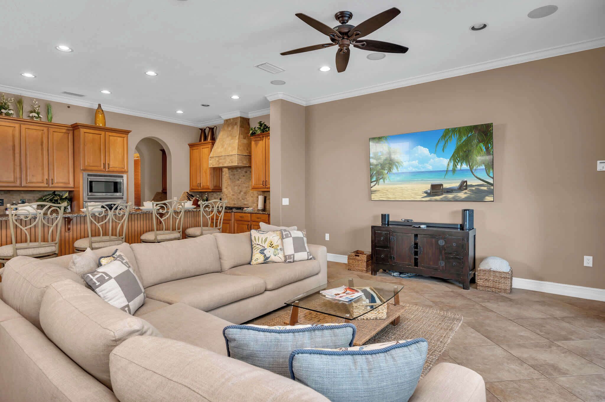 A spacious living room with a large beige sectional sofa, a glass coffee table, and a ceiling fan.