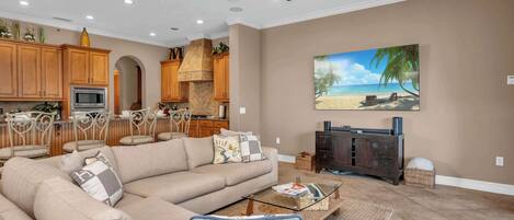 A spacious living room with a large beige sectional sofa, a glass coffee table, and a ceiling fan.