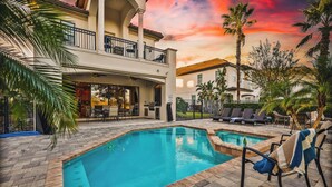 A pool area with a two-story building, outdoor seating, and palm trees. - Bright 5BR retreat w/ pool & fire pit (Kissimmee)