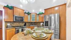 A modern kitchen with wooden cabinets, stainless steel appliances, and a round dining table set with plates and glasses. - Forget your worries in this spacious and serene space. (Miami)