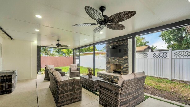 A covered patio area with wicker furniture, a stone fireplace, and a ceiling fan. - Forget your worries in this spacious and serene space. (Miami)