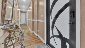 A hallway with a glass table, a decorative bowl, and a door with a unique design. - Forget your worries in this spacious and serene space. (Miami)