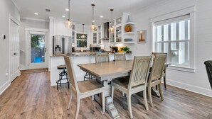 Una cocina moderna con armarios blancos, una mesa de comedor de madera e iluminación colgante.