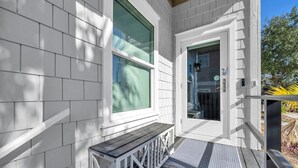 Una casa blanca con terraza de madera, un banco y una puerta con ventana.