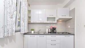 A modern kitchen with white cabinets, a stainless steel sink, a stove, and a microwave. - Welcoming Apartment With Garden (Porec)