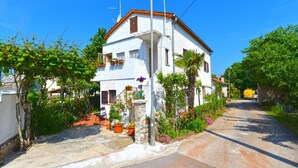 A two-story white house with a red roof, surrounded by greenery and a paved road. - Welcoming Apartment With Garden (Porec)