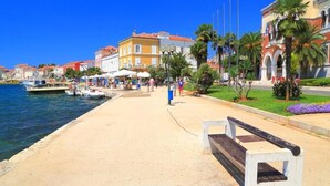A waterfront promenade with a bench, boats, and buildings along the shore. - Welcoming Apartment With Garden (Porec)