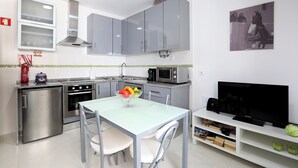 A compact kitchen with modern appliances, a dining area with a glass table, and a TV on a white stand. - T1-Sunset Apartment (Nazaré)