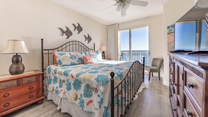 Quarto com cama, penteadeira, ventoinha no teto e vista para o exterior.