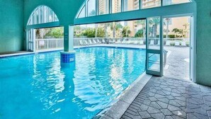 Piscina com água azul cristalina, ladeada por piso azulejado e amplas janelas em arco.