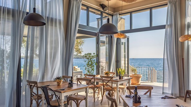 A dining area with a view of the sea, featuring a wooden table, chairs, and hanging pendant lights.