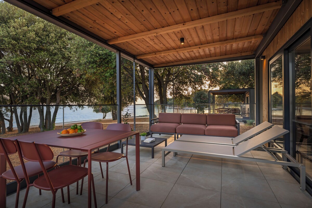 An outdoor patio with a wooden ceiling, a dining table with chairs, a sofa, and a lounge chair.